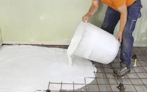 En person häller ut ett vitt material ur en stor hink över ett armeringsnät. Inspiration för betonggolv.