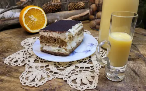 Słodki deser tiramisu, połówka pomarańczy i kieliszek likieru ze skórek pomarańczy na drewnianym blacie.