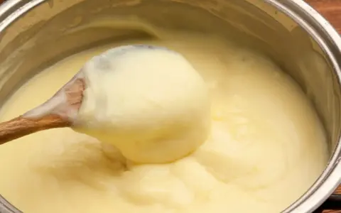 Une cuillère en bois remue une crème pâtissière maison onctueuse dans une casserole.