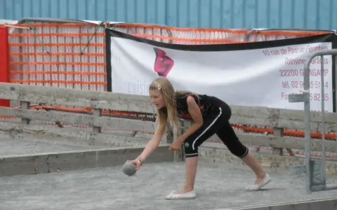 Jeune fille lançant une boule sur un terrain de pétanque, peut-être pour une partie de boule bretonne.