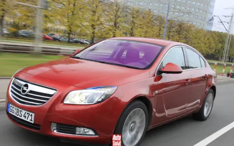 Czerwony Opel Insignia 1.6 Turbo w ruchu ulicznym. Wady tego modelu mogą dotyczyć np. spalania.