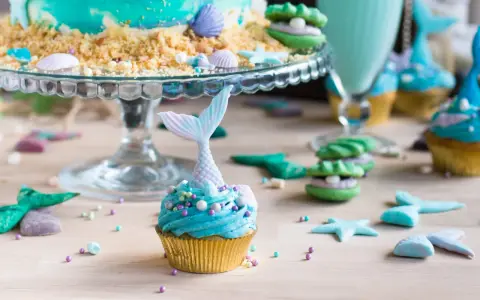 Meerjungfrau Muffins mit blauer Glasur und Schwanz-Dekorationen, umgeben von Muscheln und Seesternen.