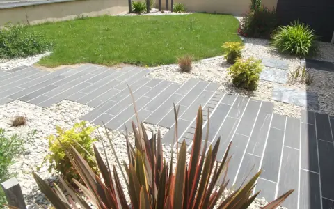 Chemin en dalles grises et gravier blanc, pelouse verte et plantes décoratives. Un jardin facile d'entretien.