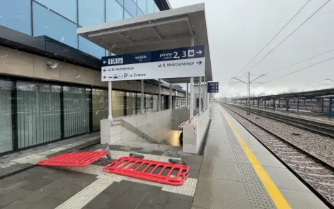 Nowoczesny dworzec kolejowy z tablicami kierunkowymi, peronami i torami w deszczu.