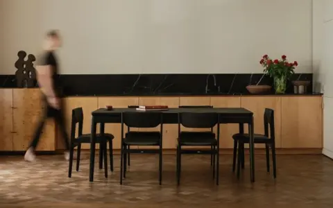 Jadalnia z czarnym stołem i krzesłami, otoczona meblami w ciepłych odcieniach dębu. W tle bukiet czerwonych róż.