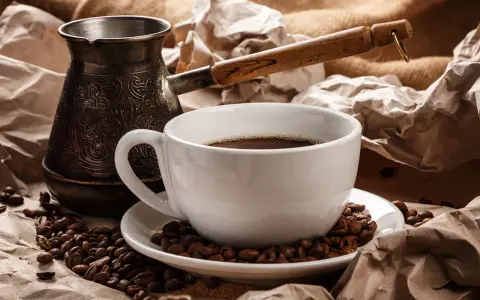 Eine Tasse heißer Espresso Mokka, umgeben von gerösteten Kaffeebohnen und einer traditionellen Mokkakanne.