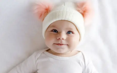 Ein süßes Baby mit blauen Augen und einer Mütze mit Bommeln. Man fragt sich, welche Augenfarbe bekommt mein Kind.