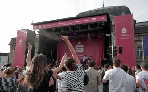 Menschen jubeln bei einem Open-Air-Konzert vor einer Bühne mit Sparkassen-Logo.