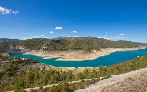 El pantano de Sacedón, con su agua turquesa, se extiende entre colinas verdes bajo un cielo azul.