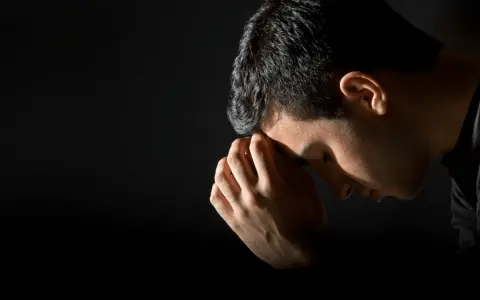 A man bows his head in prayer, hands clasped, reflecting the repentance meaning in the bible.