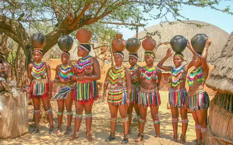Kobiety w tradycyjnych strojach niosą dzbanki na głowach. Scena z królestwa Eswatini.