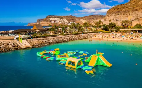 Divertimento acquatico a Gran Canaria con bambini: scivoli gonfiabili e giochi in mare su una spiaggia affollata.