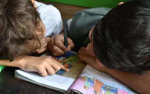 Due bambini studiano insieme, uno scrive mentre l'altro indica il libro. Un esempio di peer learning.