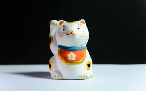 Maneki-neko blanco con detalles dorados y flor, ideal para feng shui en casa para la prosperidad.
