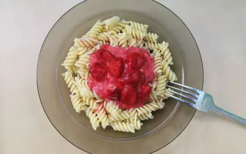 Makaron z truskawkami na talerzu, z widelcem obok.