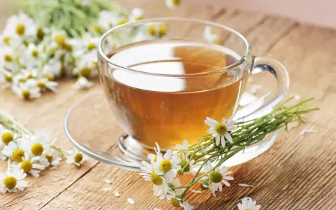 Une tasse de tisane de camomille, idéale pour le rhume traitement, entourée de fleurs fraîches sur un fond en bois.