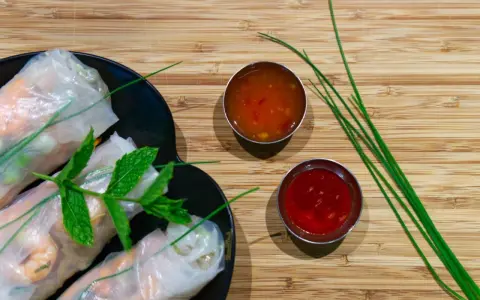 Rouleaux de printemps frais sur une assiette noire, accompagnés de deux sauces : une sauce aigre douce orangée et une sauce rouge.