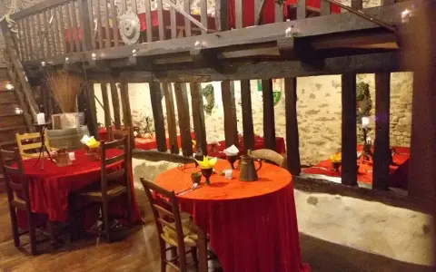 Ambiance d'une auberge moyen âge avec tables dressées de nappes rouges, poutres apparentes et murs en pierre.