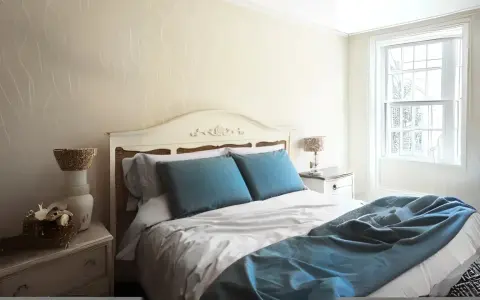 Habitación con cama matrimonial, almohadas azules y manta a juego. Las medidas de camas varían, pero esta parece cómoda.
