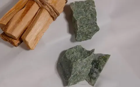 Surowe kawałki zielonego jadeitu, znanego z właściwości uspokajających, leżą obok wiązki drewna Palo Santo.
