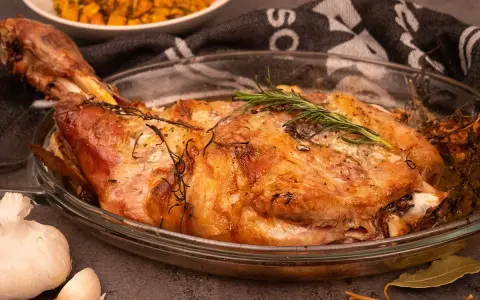 Une succulente épaule d'agneau rôtie à la perfection, garnie de romarin frais, prête à être dégustée.