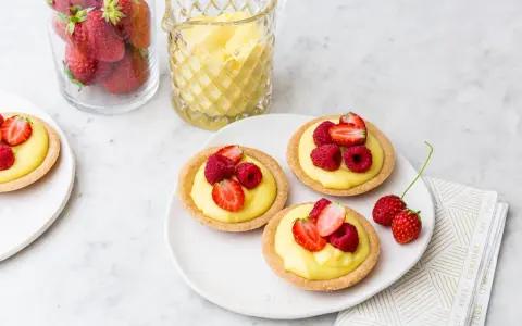 Deliziose tartellette alla frutta con crema pasticcera e frutti di bosco freschi, pronte per essere gustate.