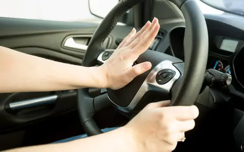 Hand drückt auf Hupe im Auto. Wann darf man hupen? Nur in Notfällen, um einen Unfall zu vermeiden.