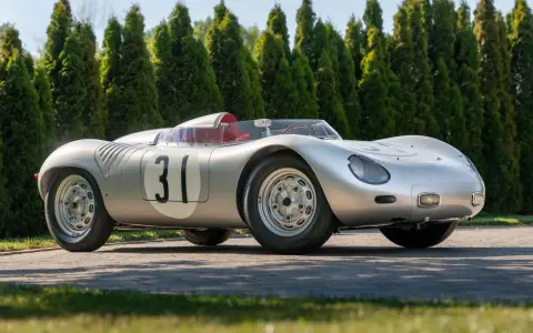 Silberner Porsche 718 RSK mit Startnummer 31, bereit für die Rennstrecke, vor einer Reihe von grünen Bäumen.