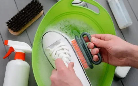 Come lavare le Superga bianche: una scarpa immersa in acqua saponata, mentre una mano la strofina con una spazzola.