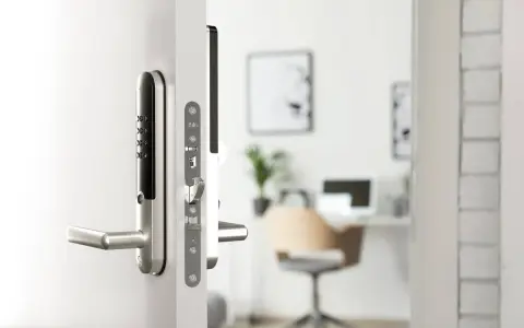 Modernt digitalt låssystem på en vit dörr. I bakgrunden syns ett kontor med skrivbord och stol.