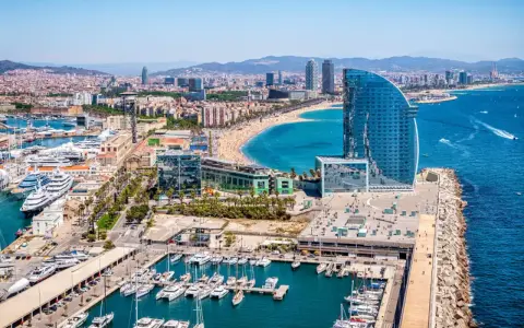 Barcelona morze: luksusowe jachty w marinie, plaża pełna ludzi i nowoczesny hotel w kształcie żagla.