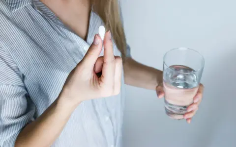 Kobieta w ciąży bierze suplement. W dłoni trzyma tabletkę i szklankę wody, dbając o odpowiednią luteinę w ciąży.