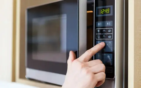 Finger drückt auf die "10" auf dem Bedienfeld einer Mikrowelle, um die Kochzeit einzustellen. Die Mikrowelle zeigt die aktuelle Uhrzeit an.