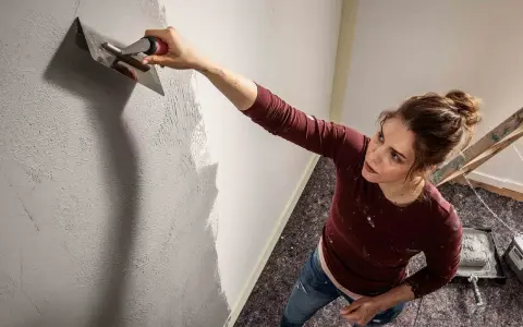 Frau trägt mit einem Spachtel eine Struktur auf die Wand auf. Die Spachteltechnik Wand verleiht dem Raum eine besondere Optik.