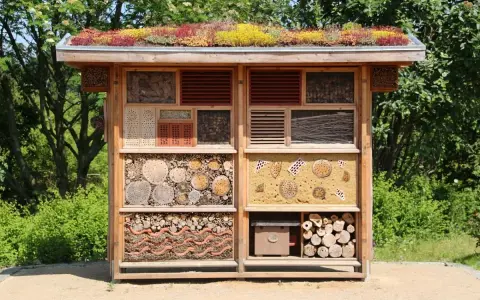 Un hotel de insectos con techo verde, lleno de materiales naturales como troncos, cañas y ladrillos, ofrece refugio a pequeños animales.