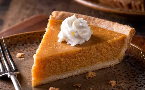 Kawałek pysznego pumpkin pie z bitą śmietaną na talerzu, gotowy do zjedzenia.