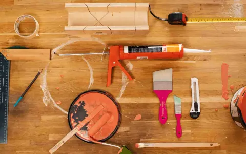 Pistolet à mastic acrylique, rouleau, pinceaux, ruban adhésif, mètre et boîte à onglets pour une utilisation en bricolage.