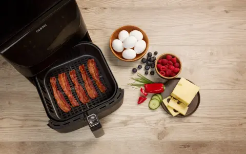 Knuspriger Bacon im Airfryer, daneben Eier, Beeren, Käse und Gemüse für ein perfektes Frühstück.