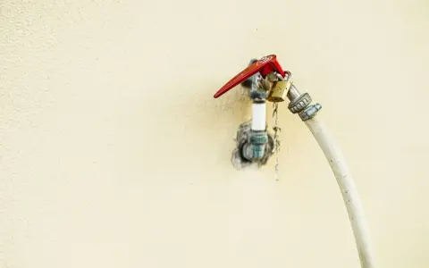 Robinet extérieur avec un cadenas doré et un tuyau blanc, le raccord asymétrique suggère une utilisation inhabituelle.