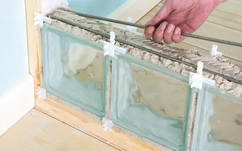 Pose de brique de verre extérieur : une main insère des barres de renfort dans le mortier entre les briques de verre, en cours d'installation.