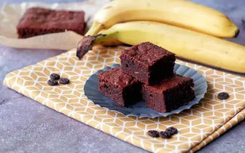 Saftige bananen brownies auf einem gelben Tuch, daneben reife Bananen.