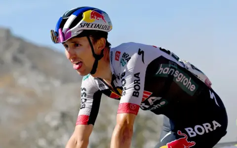 Radfahrer Jai Hindley kämpft sich mit herausgestreckter Zunge einen Berg hinauf, sein Helm trägt das Red Bull Logo.