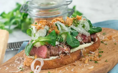 En läcker steak sandwich med saftigt kött, krispig sallad, lök och riven ost på rostat bröd.