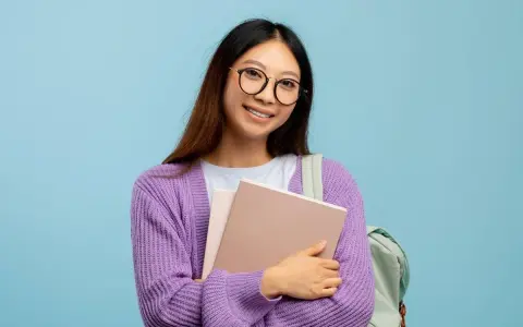 Ragazza con occhiali nuovi per astigmatismo, sorride tenendo libri e zaino.