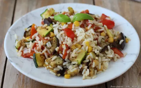 Un piatto colorato di insalata di riso vegetariana con zucchine, melanzane, pomodori e mais, guarnito con basilico fresco.