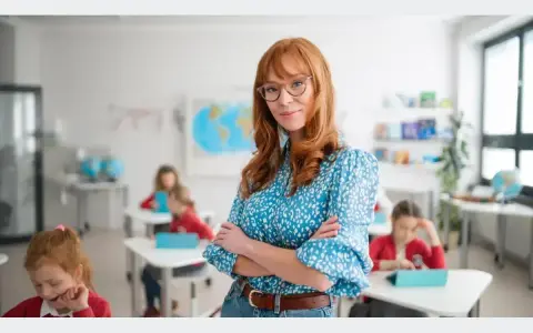 Nauczycielka w okularach z rudymi włosami stoi przed klasą. Dzieci siedzą przy ławkach. Zastanawiasz się, na jakie studia nie iść?