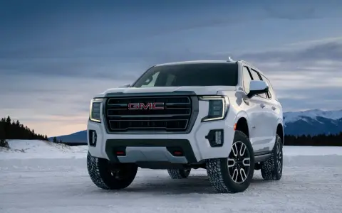 Biały GMC Yukon XL gotowy na zimową przygodę na ośnieżonej drodze, z górami w tle.