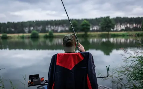 Wędkarz z klasycznym feederem czeka na branie nad spokojnym jeziorem. Jaka wędka do klasycznego feedera? Ta wydaje się idealna.