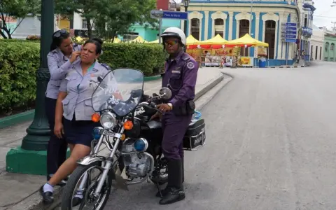 Trzy policjantki w mundurach stoją obok motocykla policyjnego na ulicy w Hawanie.