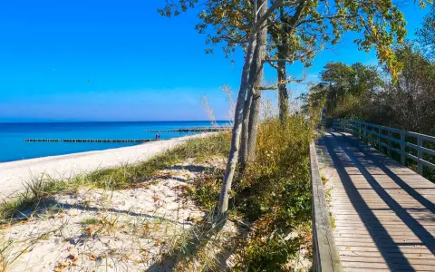 Drewniana kładka prowadząca na piaszczystą plażę nad spokojnym, błękitnym morzem.